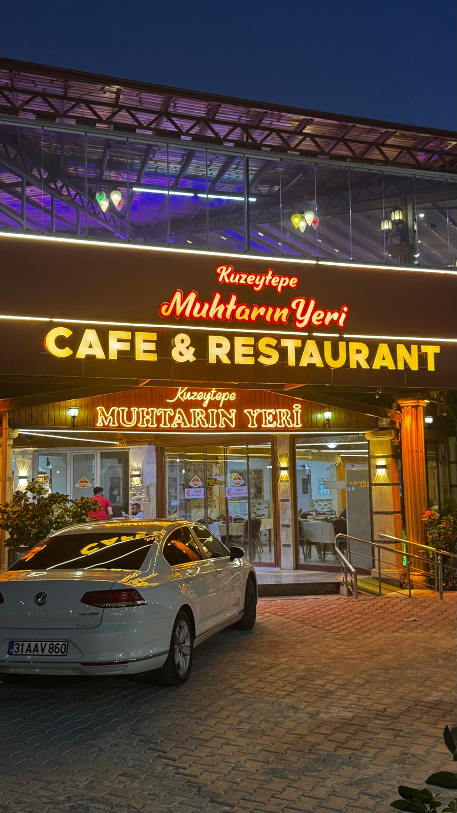 Kuzeytepe Muhtarın Yeri'nin gece ışıklandırılmış tabelası ve restoran girişi